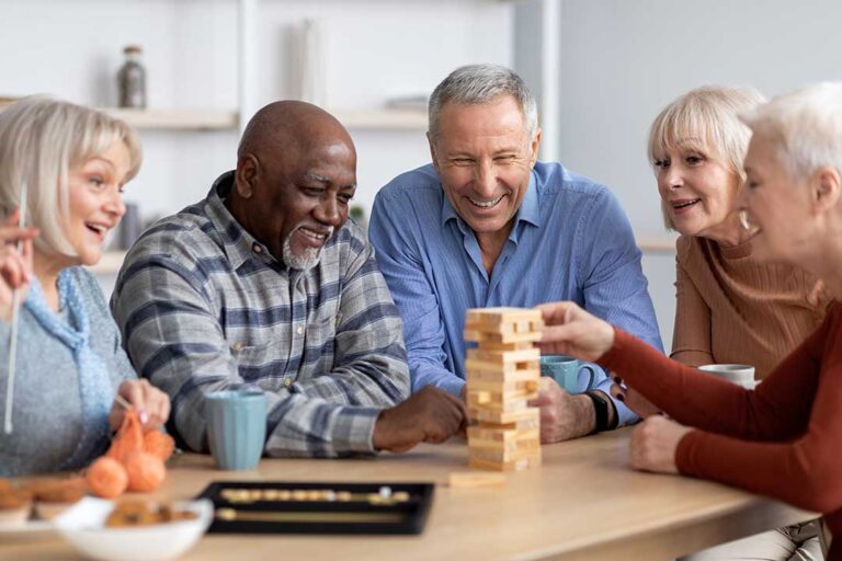 Older adults seated at a table painting, coloring, and making collages together in a bright activity room.