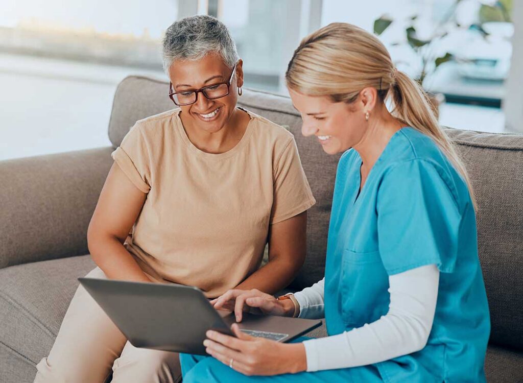 Older adult speaking with a caregiver in a bright private assisted living apartment with familiar personal belongings.